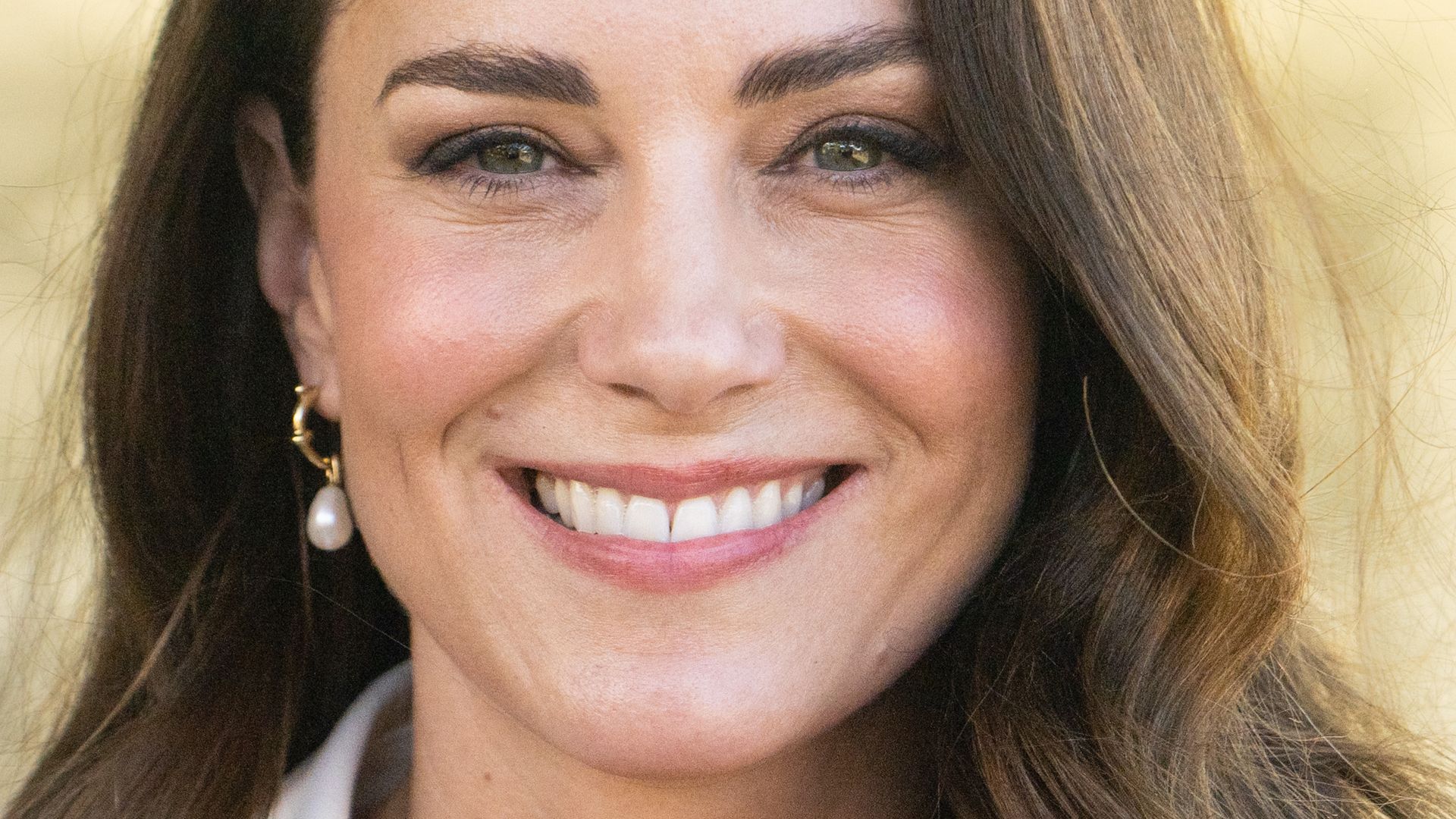 Kate Middleton, the Princess of Wales wears pearl earrings and a white blazer with orange blouse